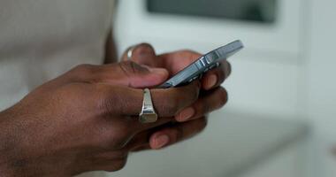 A man in casual clothes uses a mobile phone standing indoors, close-up of his hands, an unrecognizable person, daylight photo