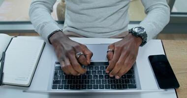 A man typing on a laptop, sitting at a table indoors, close-up of his hands, an unrecognizable person, view from above. photo