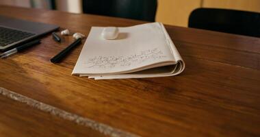 An open laptop and a notebook on a table indoors. There are no people photo