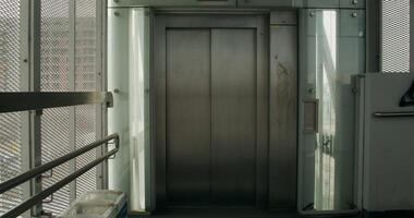 A woman in formal clothes and a coat uses a mobile phone coming out of the elevator. She's rolling a suitcase photo
