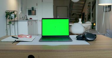 A laptop with a green screen is on the desktop at home. An open notebook and headphones next to it photo
