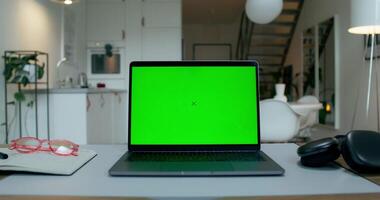 A laptop with a green screen is on the desktop at home. An open notebook and headphones next to it. A man's hand presses a laptop key photo