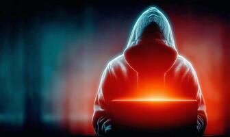 Mysterious Figure in a Hooded Sweatshirt Using a Glowing Laptop in a Dark Environment photo