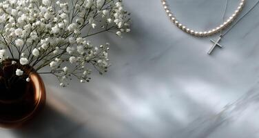 Elegant Pearl Necklace and Silver Cross Resting Beside Delicate White Flowers on a Marble Surface photo