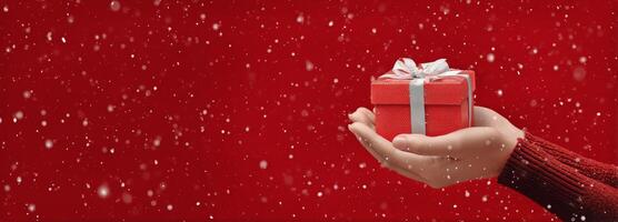 Gift Held in Hand Against Red Background With Falling Snowflakes During Winter Holiday Season photo