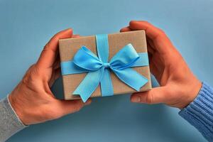 Gift Wrapped in Brown Paper With Blue Ribbon Held by Hands Against a Light Blue Background photo