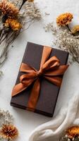 Elegant Gift Box With Brown Ribbon Surrounded by Dried Flowers on a Light Surface During Autumn Season photo