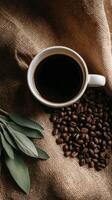Coffee Cup Surrounded by Roasted Beans and Green Leaves on Burlap Fabric photo