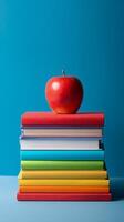 Bright Red Apple Resting on Colorful Stacked Books Against a Blue Background. photo