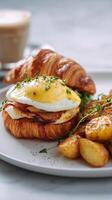 Croissant Sandwich With Eggs, Hollandaise Sauce, and a Side of Roasted Potatoes and Fruit. photo