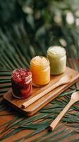 Three Vibrant Jars of Fruit Spreads on Wooden Tray Surrounded by Palm Leaves. photo
