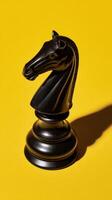 Black Chess Knight Piece on Vibrant Yellow Background Showcasing Unique Design and Shadow Details photo