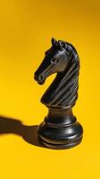 Black Chess Knight Piece Against Vibrant Yellow Background Creating Striking Visual Contrast photo
