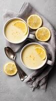 Delicious Lemon Pudding Served in Cups With Slices and Silver Spoon on Textured Grey Surface photo