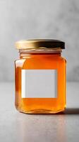 Natural Honey in a Clear Glass Jar With a Gold Lid Displayed on a Gray Background. photo