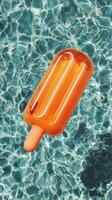 Colorful Orange Popsicle Float Resting in Clear Blue Swimming Pool Water on Sunny Day. photo