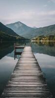 Tranquil Wooden Pier Stretching Into Calm Lake With Mountains in the Background on a Quiet Summer Morning. photo