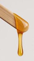 Honey Dripping From a Wooden Stick in a Bright Setting Showcasing Natural Sweetness. photo