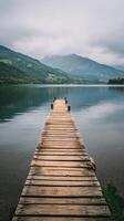 Tranquil Wooden Dock Extends Over Calm Lake Surrounded by Mountains on a Cloudy Day photo