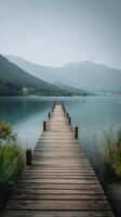 Tranquil Wooden Pier Stretching Into Calm Lake With Mountains in the Background on a Quiet Summer Morning photo