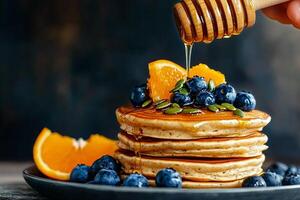 Delicious Breakfast Stack With Pancakes, Blueberries, Honey, and Orange Slices Served in Cozy Setting. photo