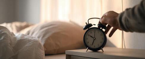 A person is reaching for an alarm clock on a bed photo