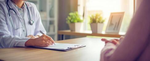 A doctor is writing on a clipboard while a patient sits at a desk photo
