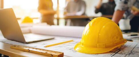 The yellow hard hat resting on architectural plans in a collaborative workspace. photo