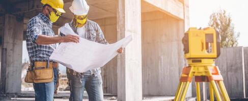 The construction workers reviewing blueprints at a site with surveying equipment. photo