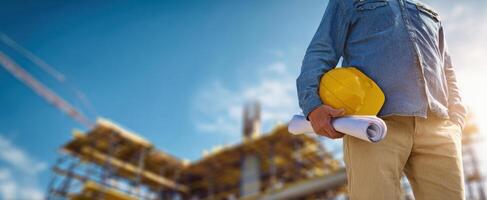 The construction worker holding plans and a safety helmet at a job site. photo