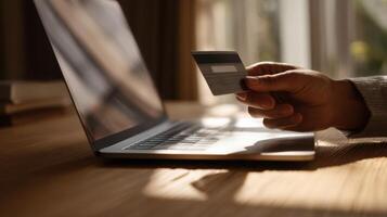The hand holding a credit card above a laptop computer on a desk. photo