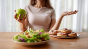 The woman choosing between a healthy apple and tempting donuts on a table. photo