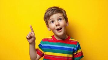 The cheerful boy with a colorful shirt pointing to an idea against a yellow background. photo
