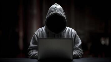 The hooded figure immersed in the glow of a laptop screen in darkness. photo