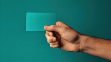 The hand holding a teal card against a minimalistic background. photo