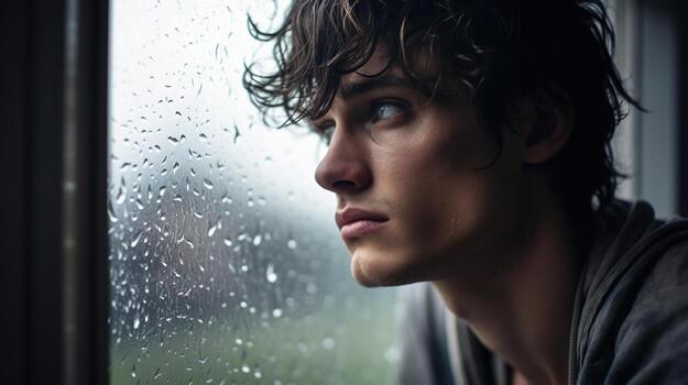A young man looking out the window with rain on the window photo