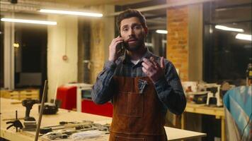 Professional Caucasian carpenter guy speaking call mobile phone in workshop artist worker wood master communicate architect male using telephone connection network man builder contact client carpentry video