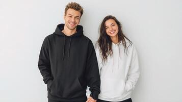 Couple wearing hoodies standing in front of white wall photo
