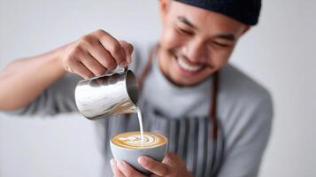 A man in an apron is pouring milk into a cup of coffee photo