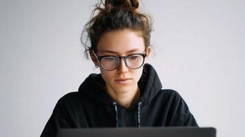 A woman wearing glasses and a black hoodie is using a laptop photo