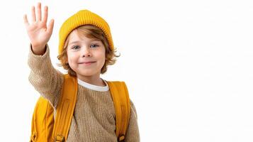 A young boy with a yellow hat and backpack waving photo