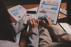 Two business people are working on a calculator and paper with graphs photo