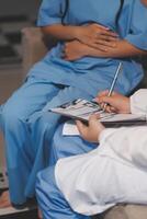 A doctor is writing on a clipboard while two nurses sit on a couch photo