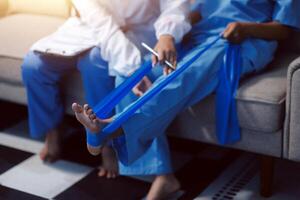 A woman in scrub clothes is sitting on a couch with a blue bandage on her foot photo