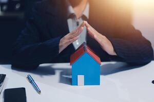 A woman is holding up a house model in front of her photo