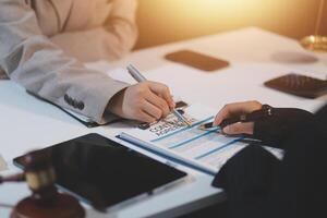 Two people are writing on a document at a desk photo