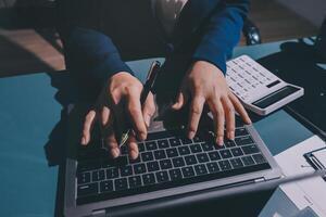 A person typing on a laptop computer with a pen and calculator photo
