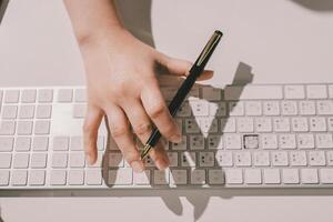 A person's hand on a keyboard with a pen photo
