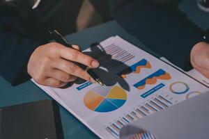 A person in a suit is holding a pen and looking at a paper with graphs and charts photo