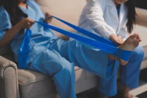 A woman in scrubs is sitting on a couch with a blue band around her leg photo